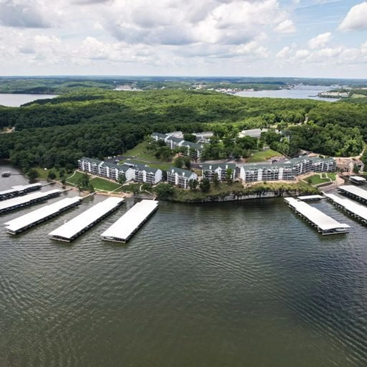 This exterior image shows a vibrant marina with boat docks, a cluster of residential buildings nestled amid lush green landscaping, and serene water stretching into the distance. The scene is inviting for outdoor activities and gatherings by the lake.