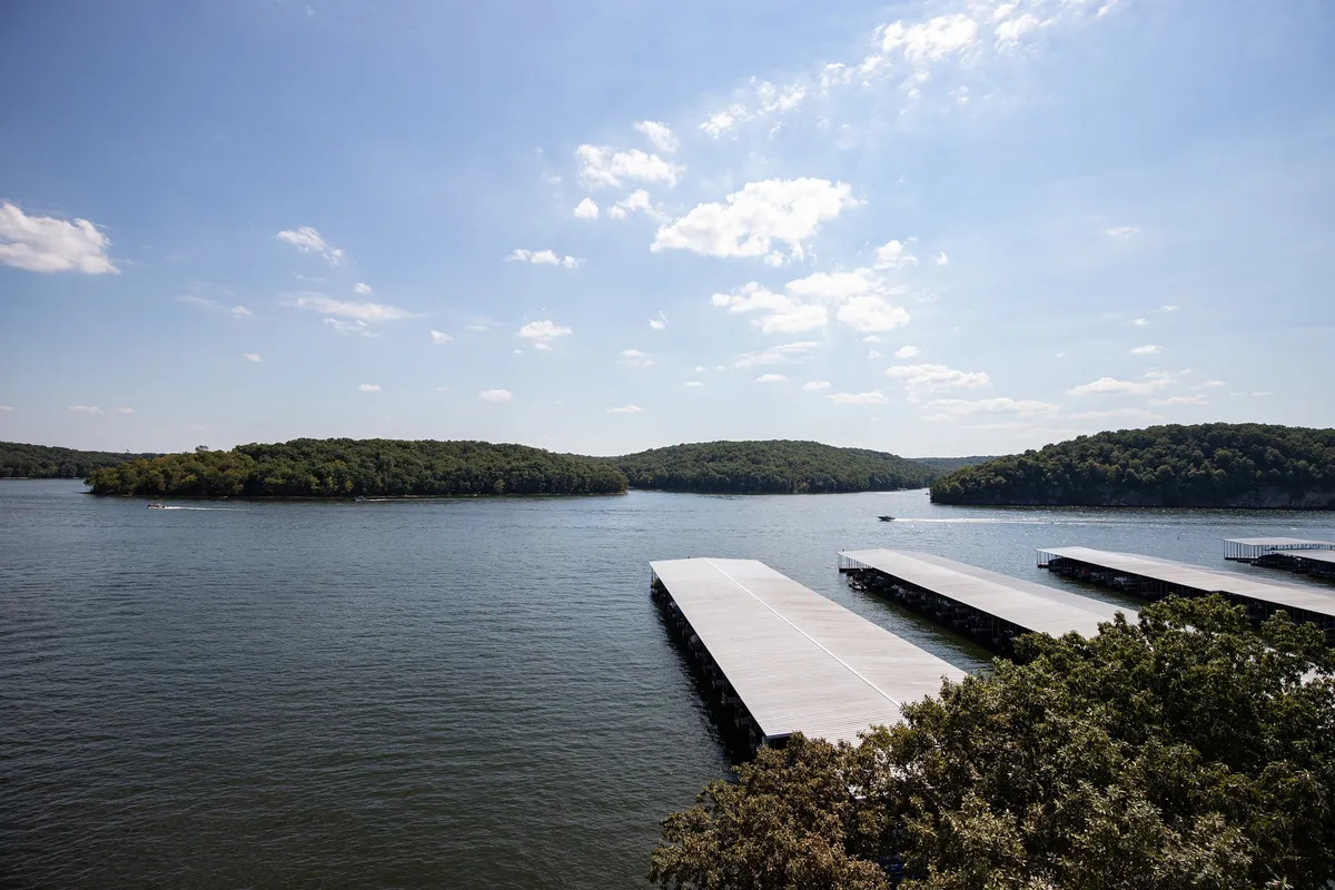 This image features a tranquil lakeside scene with docks extending into the water, small boats tied up, and distant islands beneath a bright sky. The setting exudes peacefulness and invites viewers to imagine boating, fishing, or simply relaxing by the water's edge.