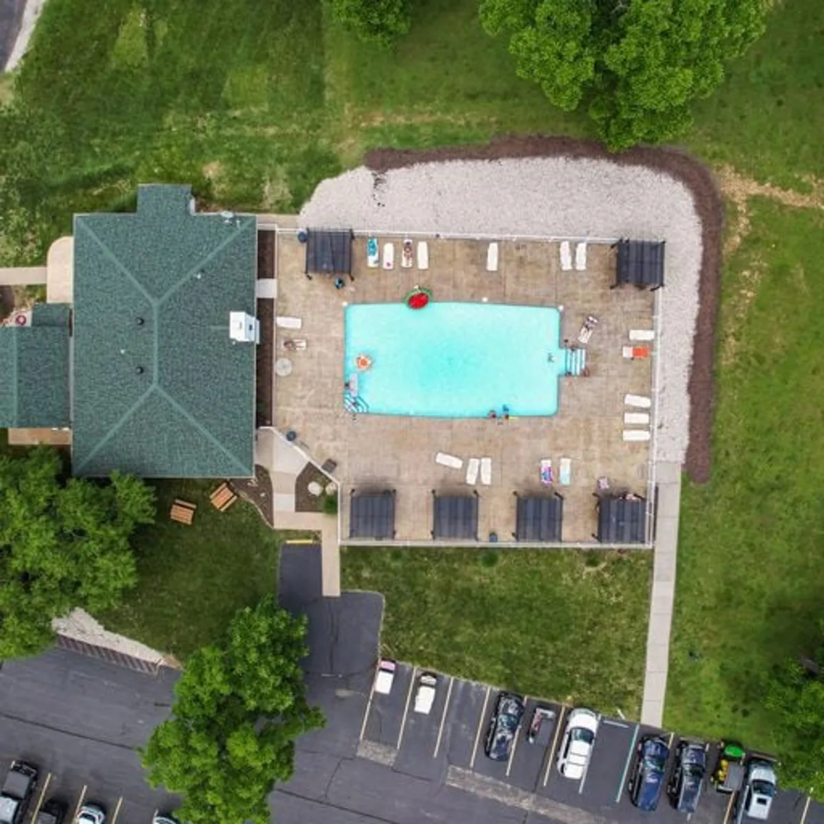 A sparkling swimming pool framed by lounge chairs and lush green landscaping, with the building visible in the background. The area is set up for relaxing, swimming, and socializing, evoking a leisurely resort atmosphere perfect for gatherings or peaceful lounging.