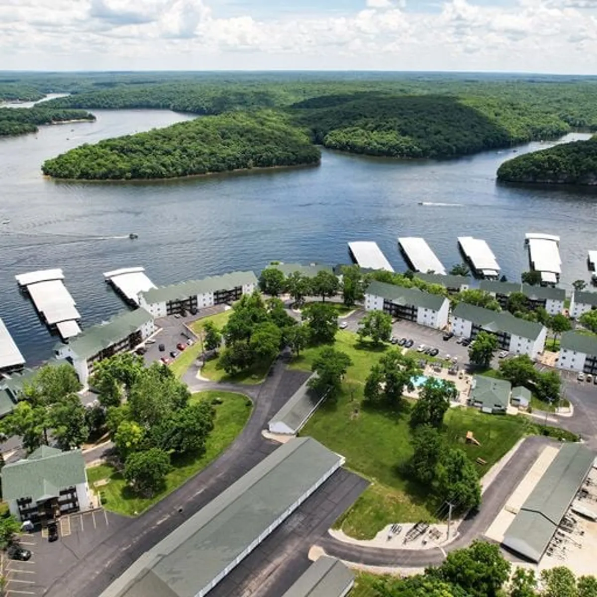 A panoramic view captures the lake, boats, green hills, residential buildings, and a swimming pool—highlighting opportunities for water activities, outdoor dining, and lakeside explorations.