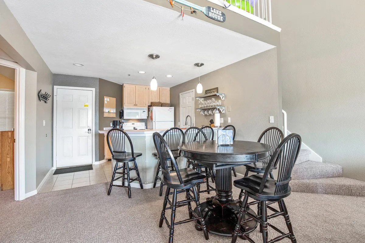 A cozy interior dining area features a round black table surrounded by bar stools and a kitchen counter, evoking a space for meals, game nights, and lively group conversations.