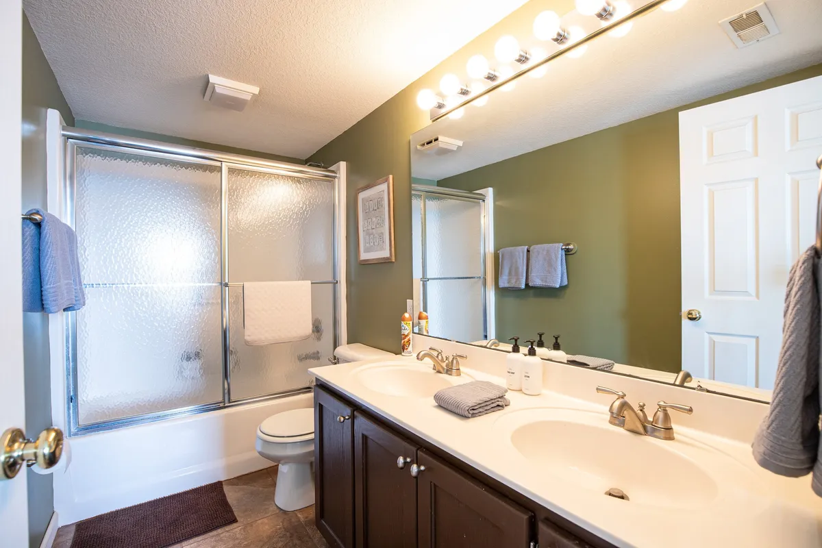 A modern bathroom with a double vanity, large framed mirror, and a glass-enclosed shower. The space is inviting and rejuvenating, ideal for personal routines and relaxation, with plenty of room for guests or families.