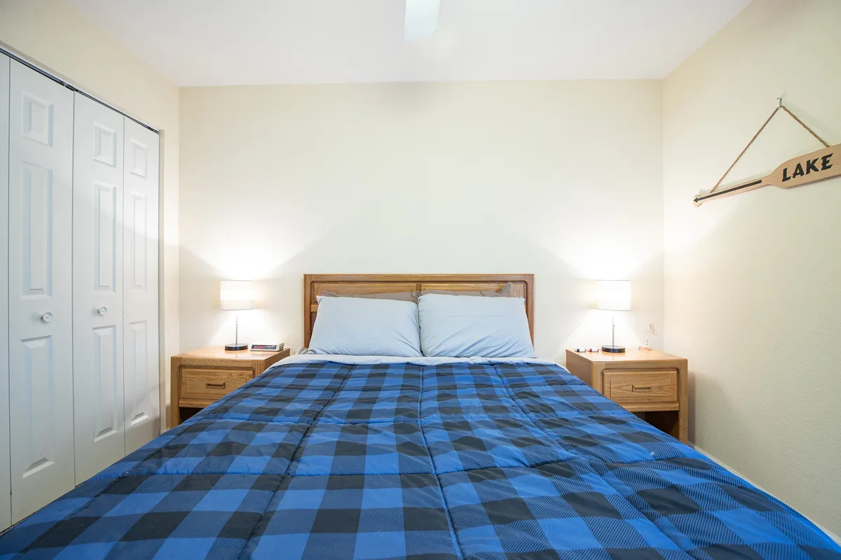 A peaceful bedroom scene with a comfortable bed, matching nightstands and lamps, and a wall sign referencing the lake. The room is bright, with soft natural light creating a restful mood, perfect for unwinding after a day by the water.